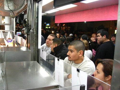 The line is four rows deep. The crowd is quite mixed, everyone loves hot dogs at midnight.
The line is four rows deep. The crowd is quite mixed, everyone loves hot dogs at midnight.
